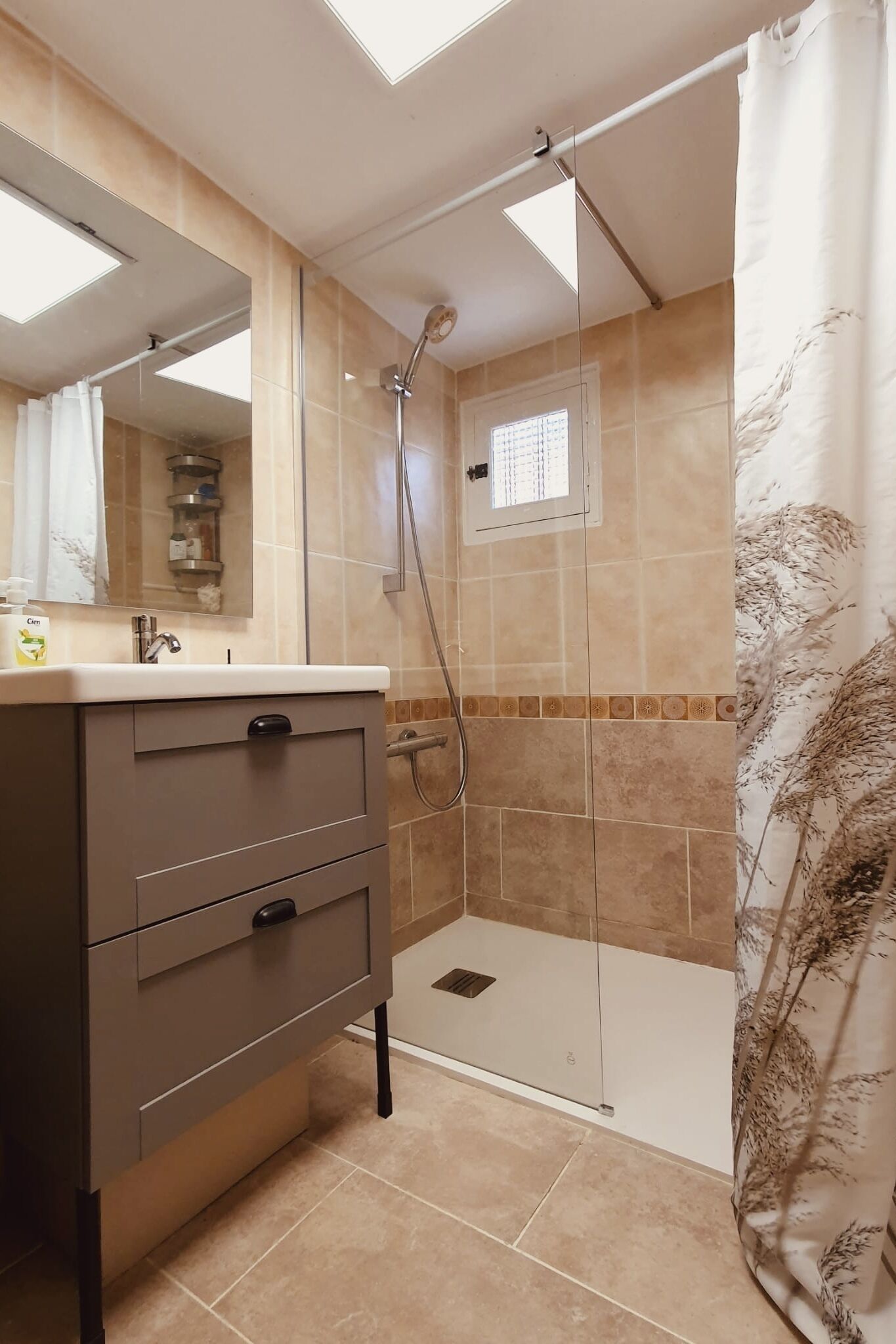 Un baño con ducha, lavabo y espejo, además de un armario.
