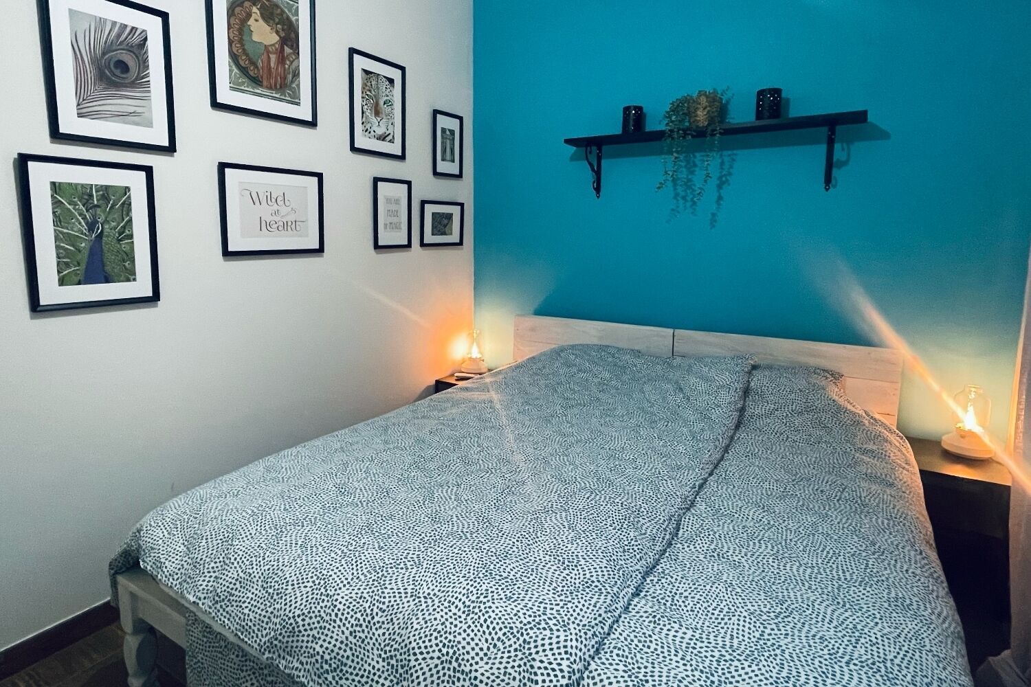 Un dormitorio con cama, obra enmarcada en la pared y repisas con adornos.