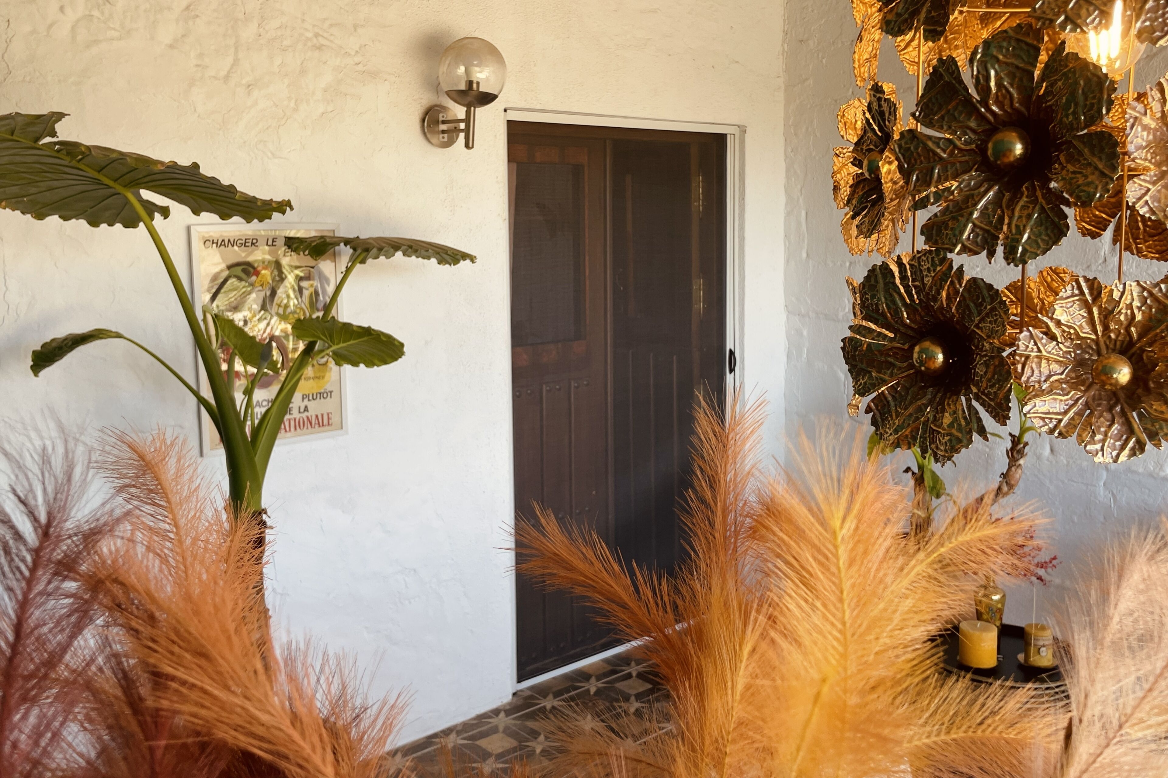 A room with a door, a wall-mounted light fixture, and decorative foliage.