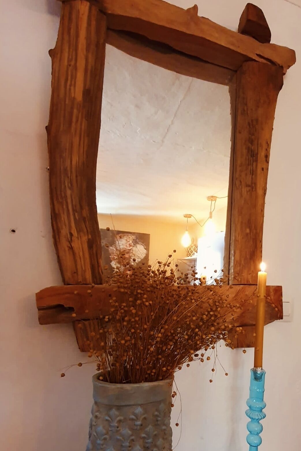 Ein rustikaler Spiegel mit Holzrahmen, eine Vase mit getrockneten Blumen und eine brennende Kerze.