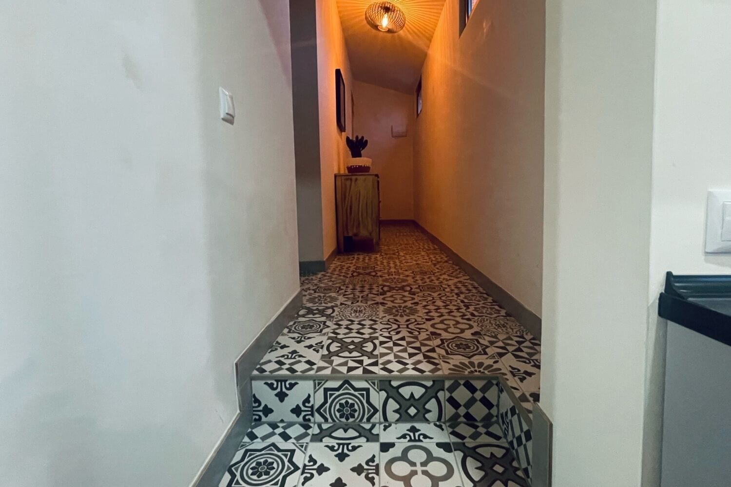 A hallway with patterned floor tiles, a light fixture, and a door at the end.