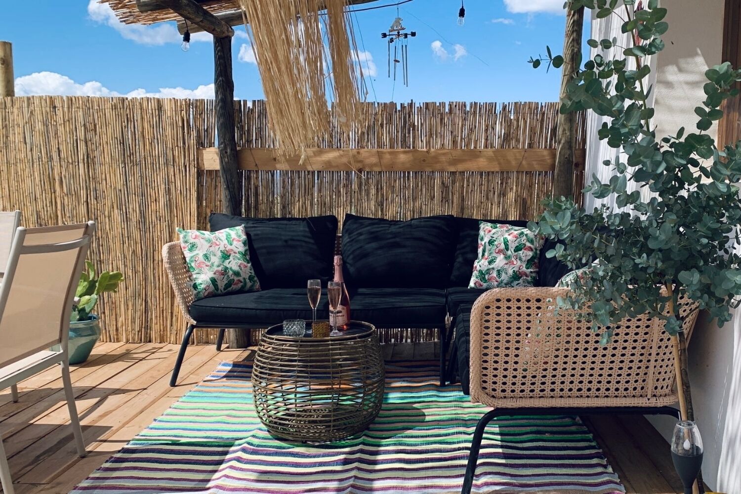 Un espacio al aire libre con un sofá negro, una mesa de centro tejida y un tapete a rayas.