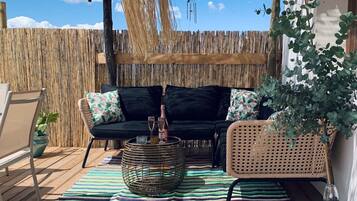 Un espacio al aire libre con un sofá negro, una mesa de centro tejida y un tapete a rayas.