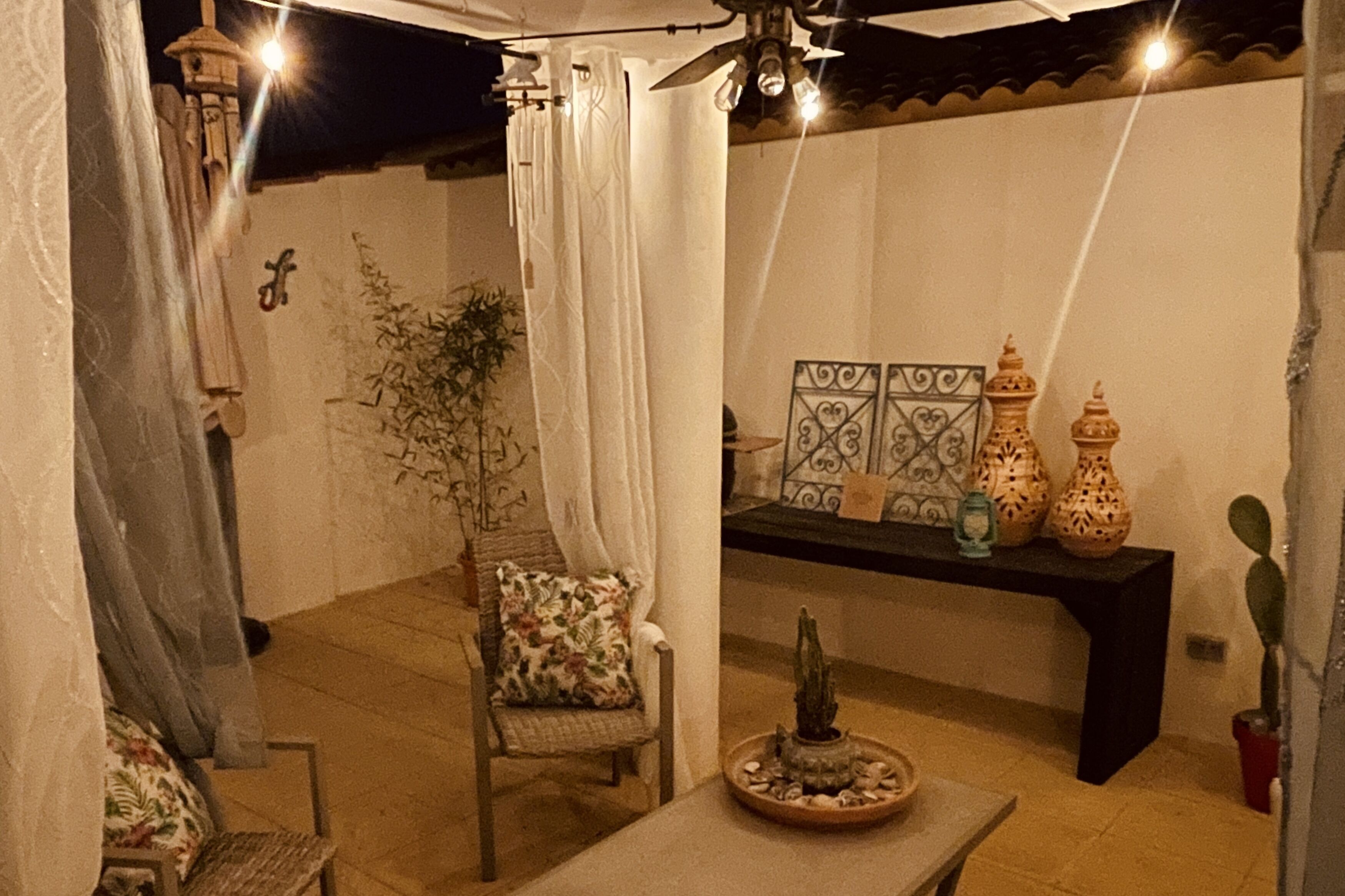 A cozy patio area with a chair, a small table, decorative vases, and a wall-mounted shelf.