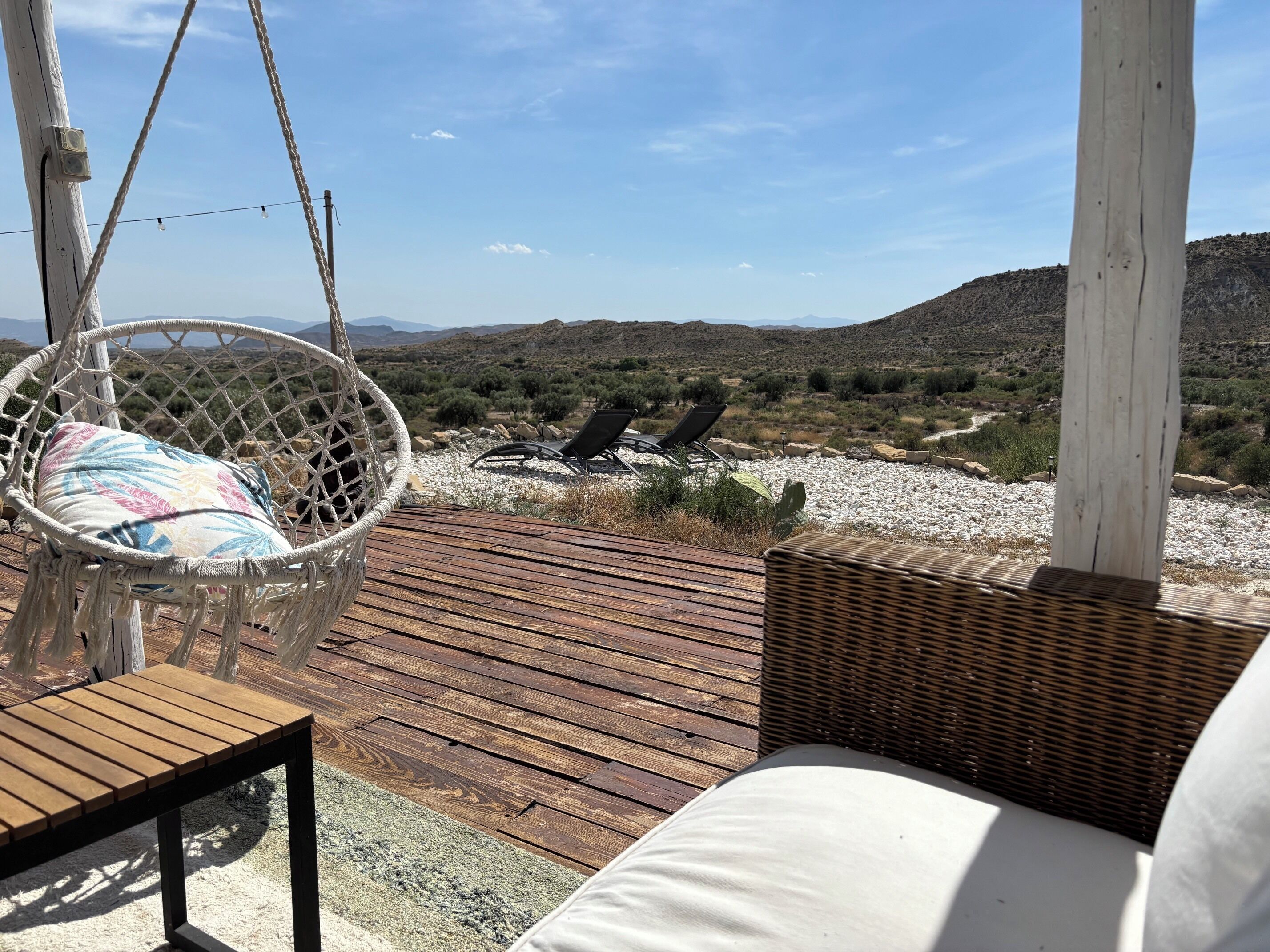 A wooden deck with a hanging chair, a wicker chair, and a table.