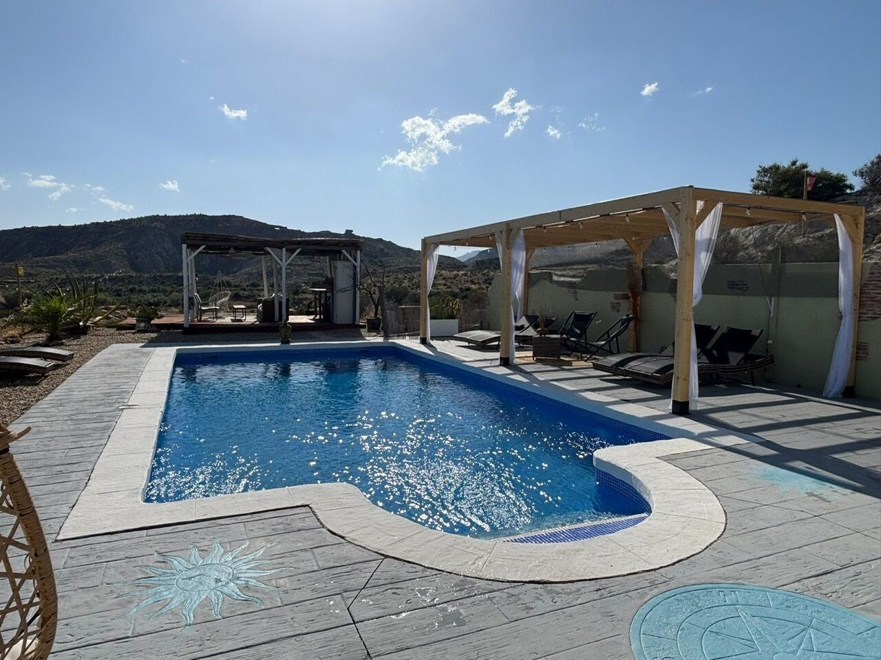 Una piscina con muelle de madera, zona de estar cubierta y montañas al fondo.