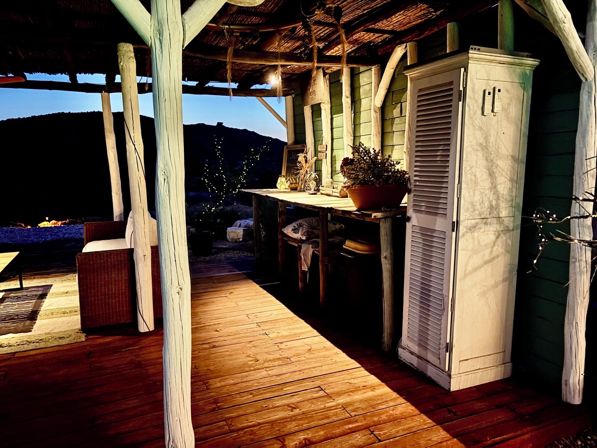 A rustic outdoor seating area with wooden furniture, a table with a potted plant, and a white cabinet.