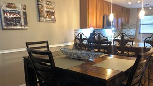A dining area with a wooden table and chairs, a decorative bowl, and a kitchen in the background.
