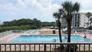 A swimming pool with a white fence, palm trees, and a building in the background.