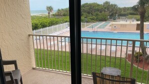 A balcony with a view of a swimming pool, a white fence, and a palm tree.