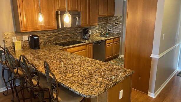 A kitchen with granite countertops, wooden cabinets, a stainless steel refrigerator, a coffee maker, and pendant lighting.