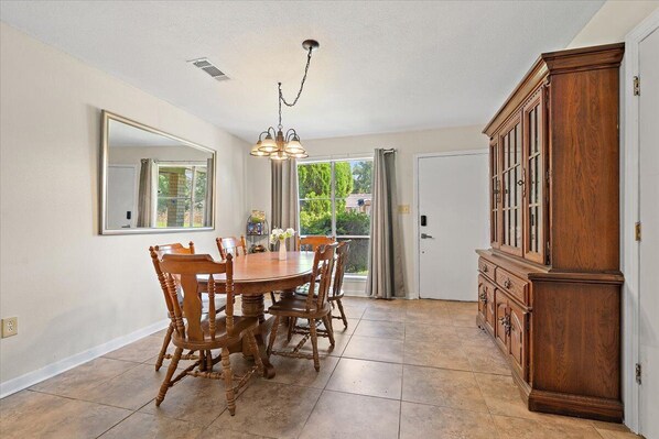 A dining room with a wooden table and chairs, a chandelier, and a large wooden cabinet. - Spacious House w/ Jacuzzi Tub (Zachary)