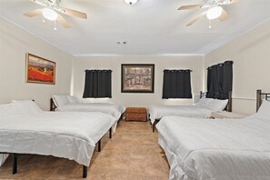 A hotel room with four single beds, a ceiling fan, two paintings on the walls, and a small ottoman in the center. - Spacious House w/ Jacuzzi Tub (Zachary)