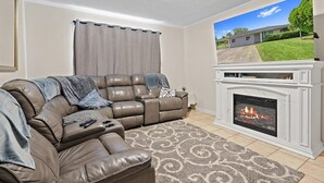 Ein Wohnzimmer mit einem braunen Ledersofa, einem Kamin und einem Fernseher, der eine Außenansicht eines Hauses zeigt.