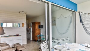 A modern room with a sliding glass door leading to a balcony, a dining area with a table set for two, and a kitchenette with a refrigerator and a microwave.