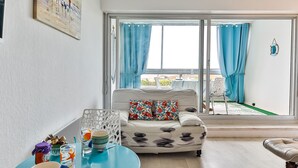 A living room with a sofa, a round table with decorative items, and a view of the outside through large windows.