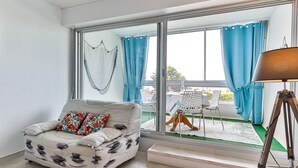 A modern living room with a sofa, a dining table with chairs, and a large window with curtains.