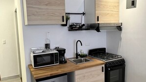 Una cocina compacta equipada con microondas, cafetera, pileta, estufa y refrigerador.