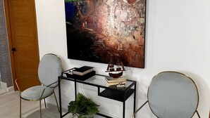 A modern room with a large abstract painting, a glass desk, two chairs, and a potted plant. - Suites By Salcedo 3 (Santo Domingo)