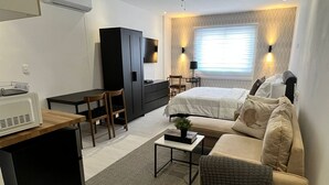 A compact hotel room with a bed, a sofa, a desk, and a kitchenette. - Suites By Salcedo 3 (Santo Domingo)