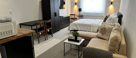 Ett kompakt hotellrum med en säng, en soffa, ett skrivbord och ett litet kök.