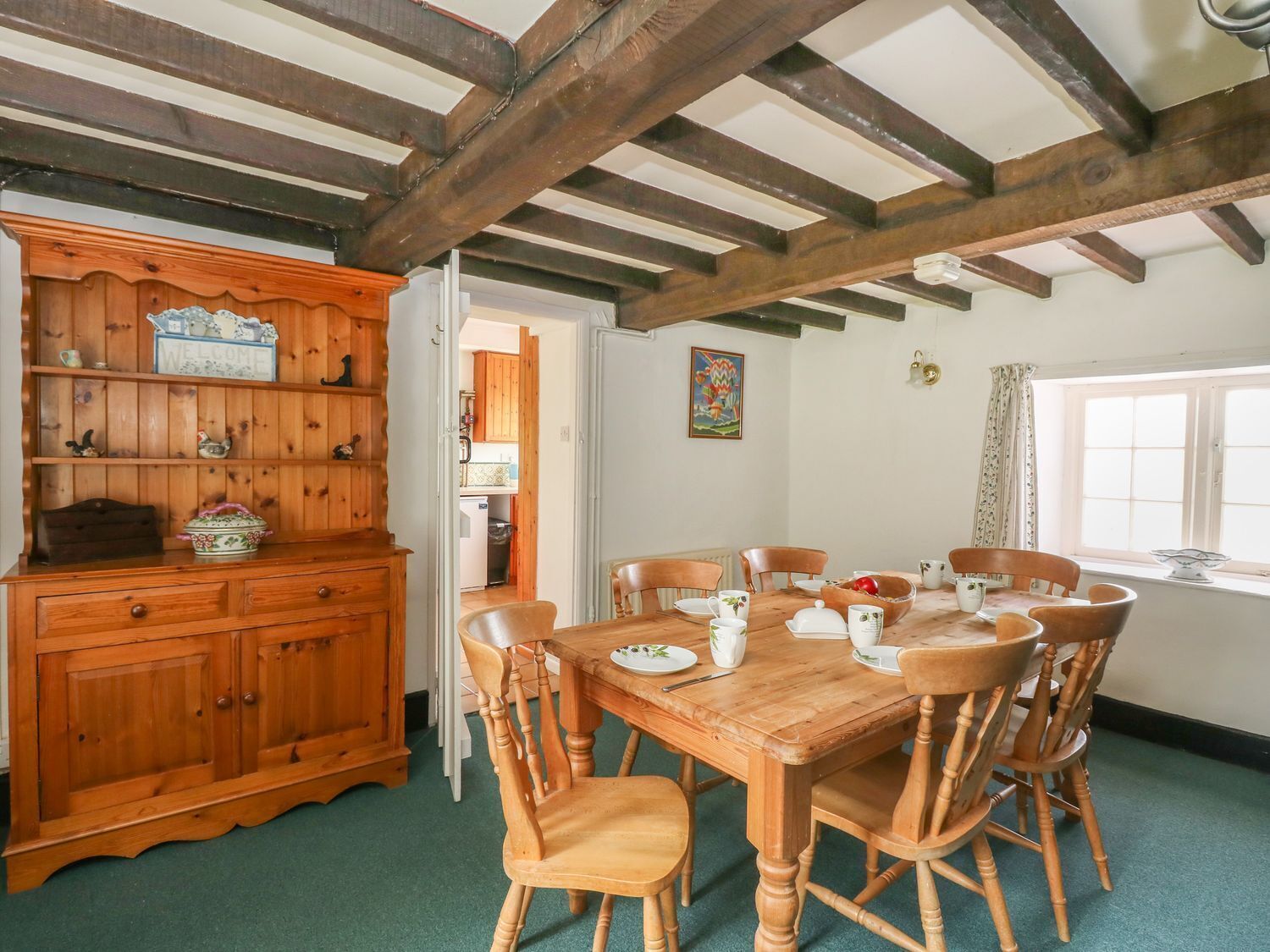 Un coin repas avec une table et des chaises en bois, un meuble en bois avec des étagères et une fenêtre avec des rideaux.
