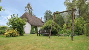Een huis met rieten dak en een schommel in een gazon.