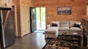 Interior de una cabaña de madera con un sofá, una mesa de centro y un refrigerador.