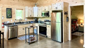 Interior de una cabaña de madera con cocina que incluye electrodomésticos de acero inoxidable, armarios de madera y un pequeño comedor.