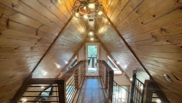 Une pièce mansardée en bois, avec un plafond en pente, un luminaire central et une vue sur l’extérieur par une fenêtre.
