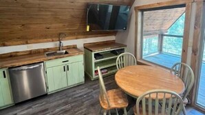 Une cuisine avec des meubles en bois, un lave-vaisselle en acier inoxydable, une table à manger en bois avec des chaises, et un téléviseur fixé au mur.