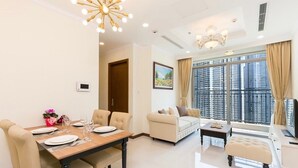 A modern living room with a dining area, large windows, and a view of high-rise buildings.