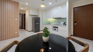 A modern kitchen with white cabinets, a built-in microwave, and a black refrigerator. There is a round dining table with a potted plant in the center.