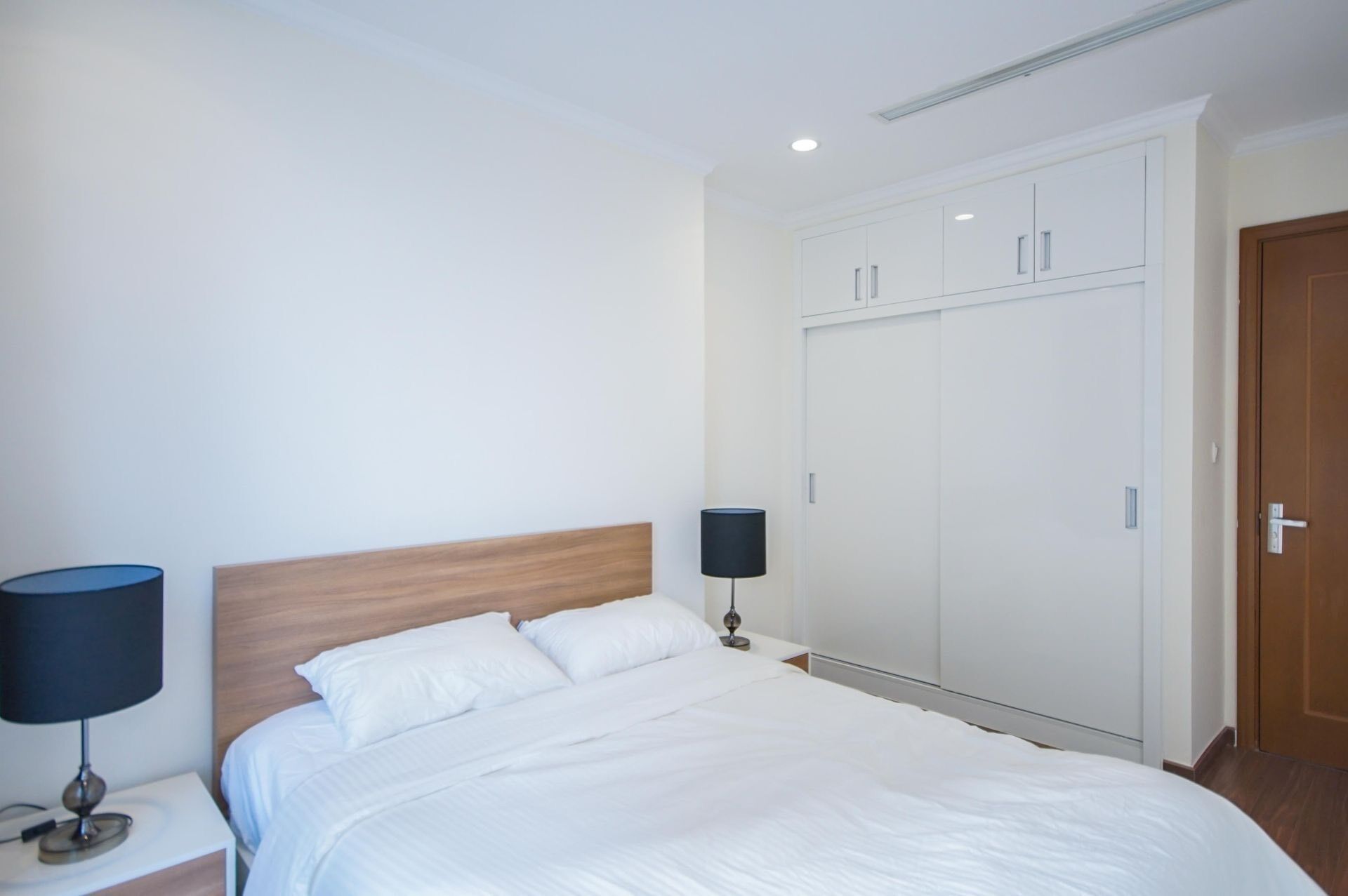 Une chambre à coucher avec un lit, une table de chevet avec une lampe, une armoire et une porte.