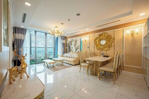 A modern living room with a sofa, dining table, and chairs, large windows, and decorative wall art. - Vinhomes Central Park (Ho Chi Minh City)