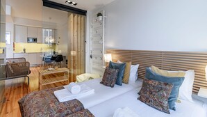 Una moderna camera d'albergo con un letto grande, una testata in legno, un'area relax con tavolo e sedie, e un angolo cottura.