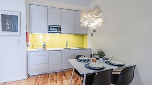 Una cucina compatta con mobili bianchi, un forno a microonde e un lavello. È presente un tavolo da pranzo apparecchiato con piatti, bicchieri e posate.