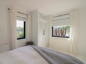 A bedroom with a bed, two windows with curtains, a radiator, and a wardrobe. - West Island (Kingsbridge)