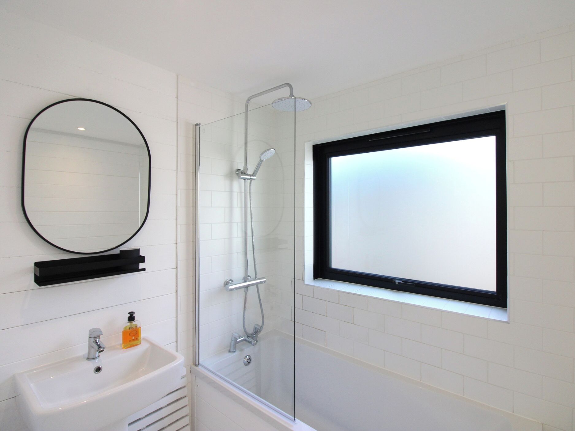 Un baño con lavamanos blanco, espejo, cabina de ducha y ventana con vidrio esmerilado.
