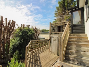 A wooden deck leading to a building with a window, surrounded by greenery and a fence. - West Island (Kingsbridge)