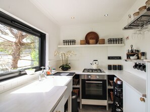 A modern kitchen with white cabinetry, a gas stove, an oven, and a window with a view of trees.