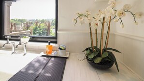 Une salle de bain avec une grande fenêtre, un lavabo, un miroir et une plante orchidée en pot.