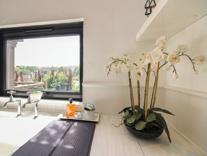 A bathroom with a large window, a sink, a mirror, and a potted orchid plant. - West Island (Kingsbridge)