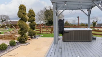 A wooden deck with a hot tub and string lights, surrounded by a stone wall and a wooden fence.