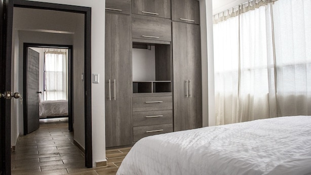 Un dormitorio con una cama grande, un armario con varios cajones y una puerta que da a otra habitación.