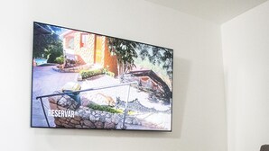 Una sala de estar con un televisor de pantalla plana montado en la pared mostrando un anuncio de propiedad. Hay un sofá gris y una mesa de centro con una cesta y un jarrón.
