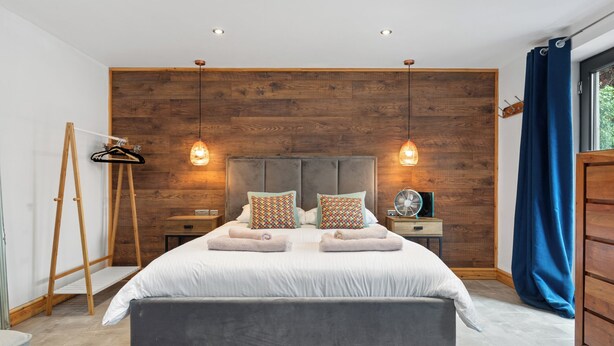 Un dormitorio moderno con una cama grande, paneles de madera en la pared y dos lámparas de noche.