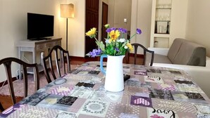 A dining area with a table covered in a patchwork tablecloth, a white pitcher with flowers, and a television on a stand. - In the greenery of Rome, near Trastevere and the Vatican (Roma)