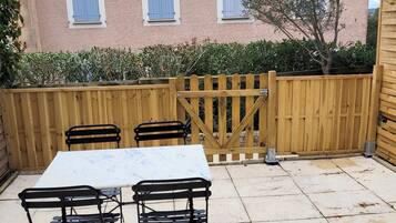 Eine Terrasse mit Tisch und Stühlen, ein Holzzaun und ein Gebäude mit Ziegeldach im Hintergrund.