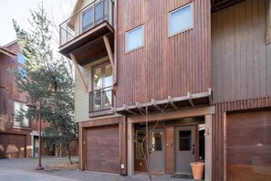 A modern multi-story building with a wooden facade, a balcony on the upper floor, and a garage door.